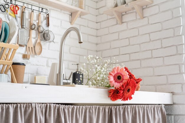 Rustic white kitchen interior with red fresh gerbera flowers inside the sink