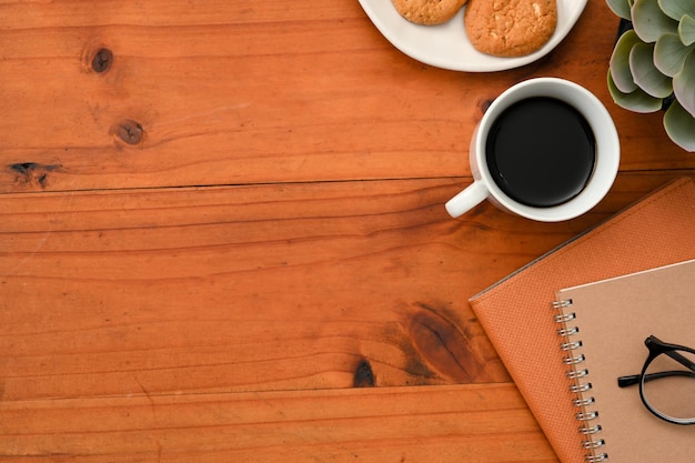 Rustic wood table background with copy space coffee cup cookies notebook and eyeglasses top view