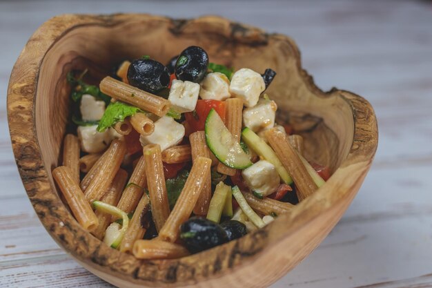 A rustic wooden bowl containing a Mediterranean pasta salad