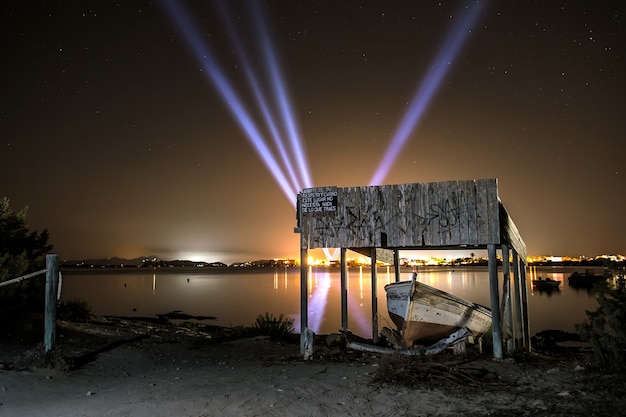 rustic wooden jetty with light cannons on the horizon from a town lit up at night