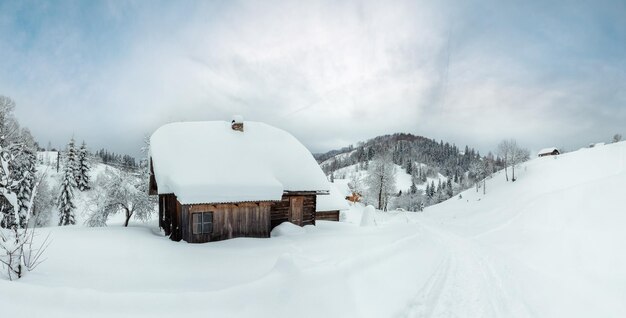 Rustiek houten huis in sneeuwbanken op de hellingen in de winter Oekraïense Karpaten bij bewolkt weer