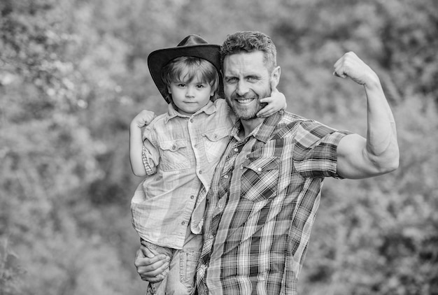 Rustieke familie Groeiende schattige cowboy Kleine helper in de tuin Kleine jongen en vader op de achtergrond van de natuur Geest van avonturen Sterk als vader Kracht als vader Kind plezier cowboy vader