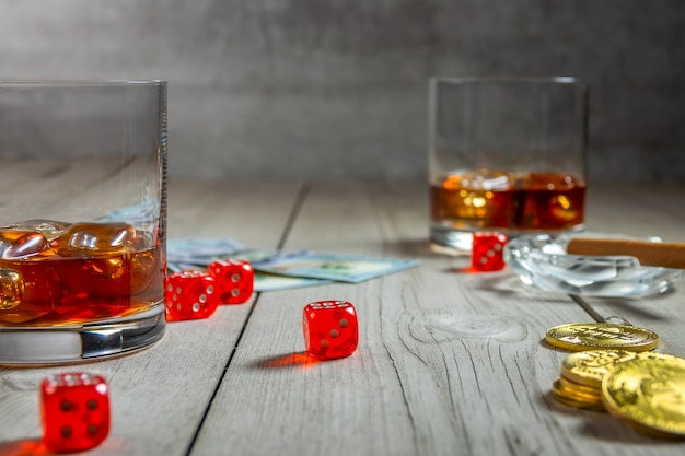 Rustieke houten tafel. Twee glazen whisky met ijsblokjes en een sigaar in een asbak. Dollarbiljetten en dobbelstenen. Een paar bitcoin-munten