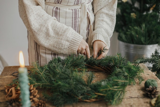 Rustieke kerstkrans maken vrouw handen houden ceder takken vast en maken krans op houten tafel