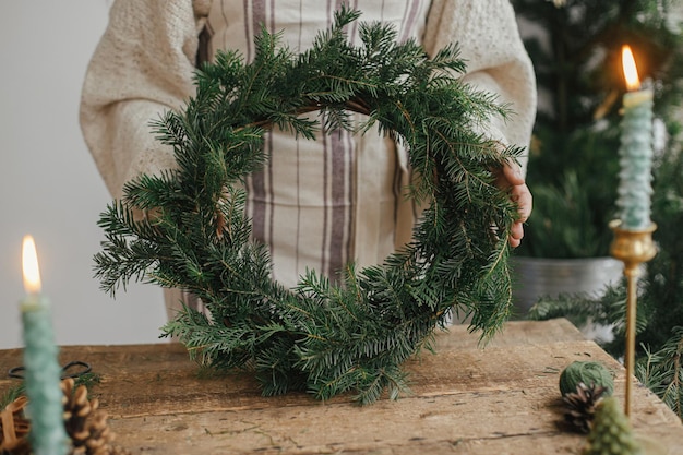 Rustieke kerstkrans maken Vrouw met stijlvolle kerstkrans aan rustieke houten tafel