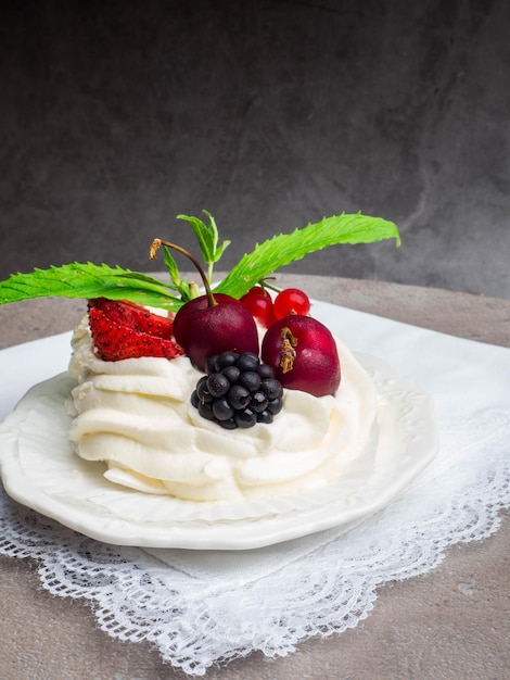 Rustieke Pavlova-cake met verse aardbeien, kersen, bramen, munt en slagroom op een betonnen achtergrond