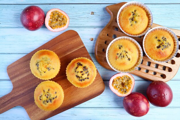 Rustieke stijl zelfgemaakte passievruchtenmuffins op broodplank met verse rijpe passievruchten op lichtblauwe houten tafel