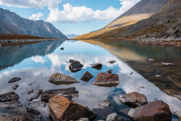 Rustig herfstlandschap met wolken reflectie op glad spiegeloppervlak van bergmeer in hooghangende vallei Meditatief uitzicht van kalm bergmeer naar uitgestrekte bergen Stenen in helder water