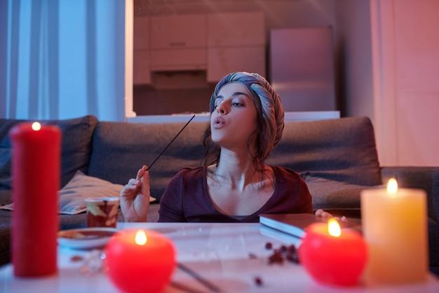 Rustige mooie donkerharige vrouw met hoofddeksels blazend op een wierookstokje in haar hand