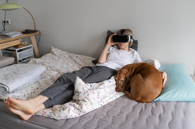 Rustige scandinavische vrouw van middelbare leeftijd die 's ochtends in het weekend geniet van videogames met hond