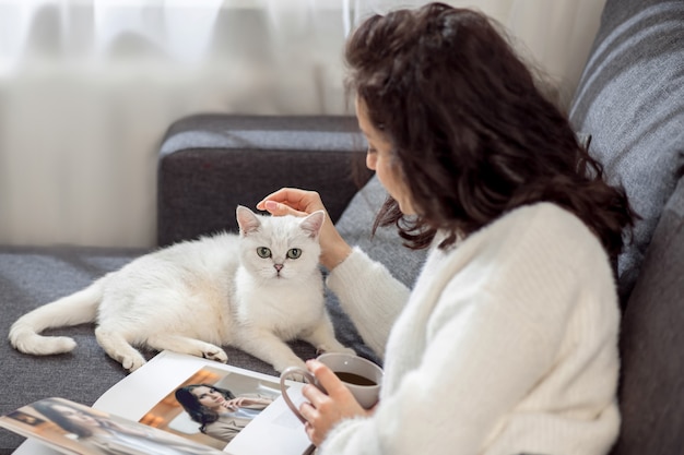 Rustige sfeer. Een vrouw die thuis rust, tijdschriften leest en haar kat aait