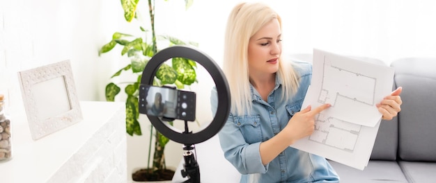 Rustige slimme vrouw die in de slaapkamer voor een camera op statief staat en een rol papier vasthoudt.