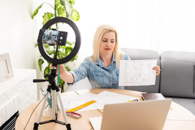 Rustige slimme vrouw die in de slaapkamer voor een camera op statief staat en een rol papier vasthoudt.