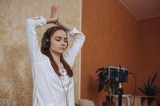 Rustige vrouw in oortelefoons die naar les luistert en yoga-oefeningen doet tijdens het oefenen thuis