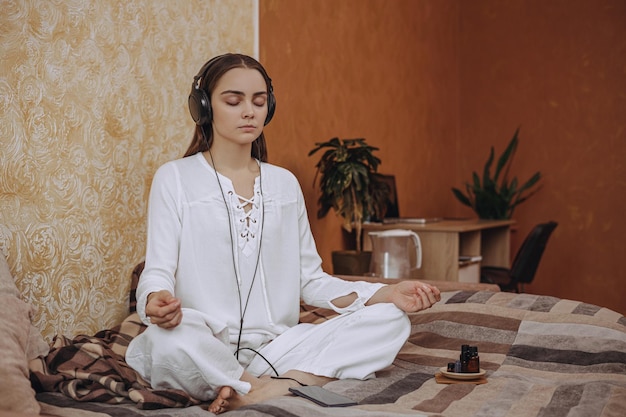 rustige vrouw met gekruiste benen die yoga doet in lotushouding en luistert naar meditatie