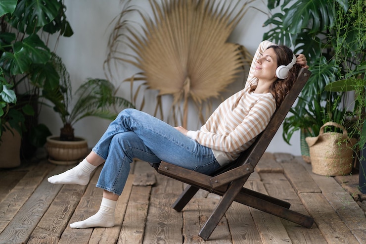Foto rustige vrouw zittend in een fauteuil in een gezellige kas dromend rustend naar muziek luisteren op de koptelefoon