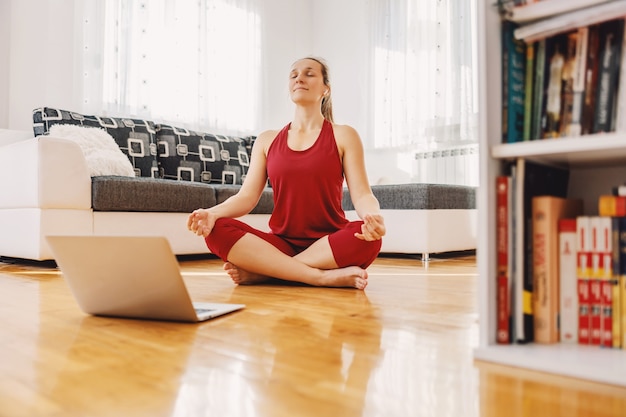 Rustige yoga-instructeur zittend in lotus yoga pose op de vloer thuis en met een online les.