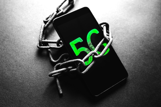 Rusty chains around the smartphone with 5g sign. Addicted to modern technologies.