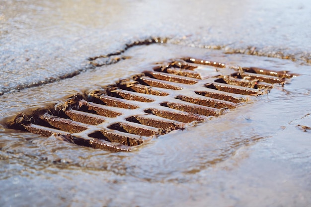 The rusty grate of the storm sewer after the rain The water drains into the storm drain Selective focus defocused background