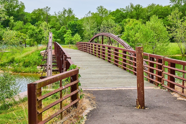 Rusty iron metal walking bridge with yellow paint on pole leading to Canadian geese on grass