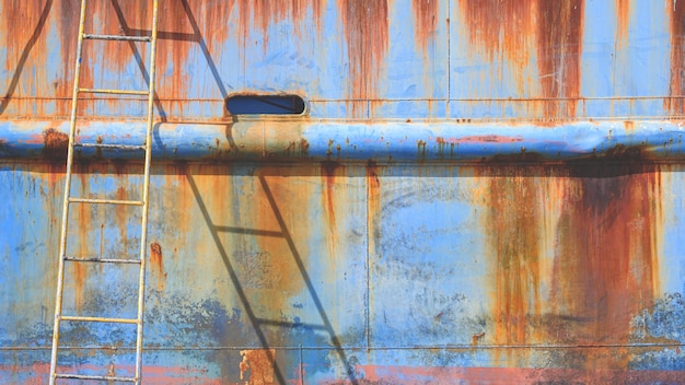 Фото Ржавый металлический корпус старого морского судна с лестницей на верфи во время ремонтных работ