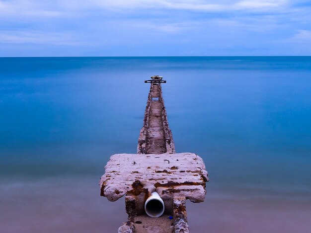 Rusty metallic structure by sea against sky