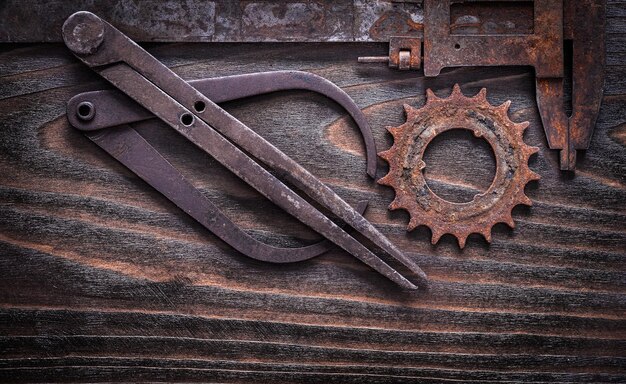 Rusty obsolete measuring calipers with gear wheel on vintage dark wooden surface construction concept