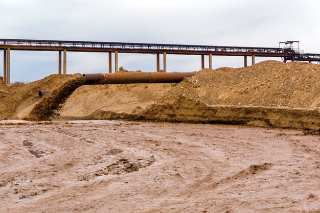 Фото Ржавая труба на берегу реки, из которой стекают сточные воды, грязная песчаная жижа