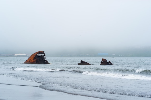 Rusty shipwreck remains of a ship washed ashore against a foggy seashore