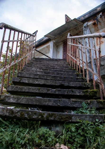 Photo rusty staircase of an abandoned building overgrown with grass and moss