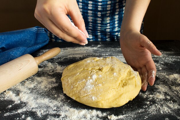 Ruw deeg voor baksel en vrouwenhanden op de donkere achtergrond