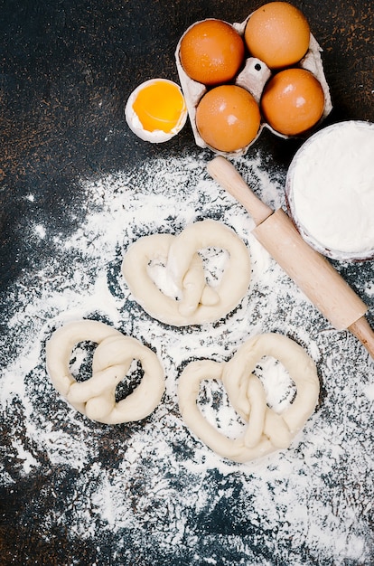 Ruw gistdeeg in kom en ingrediënten, eieren, bloem, korenaren op donkere lijst