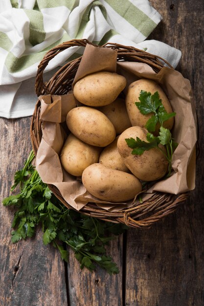 Ruwe biologische aardappel met peterselie in mand op houten tafelblad bekijken