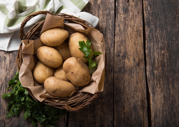 Ruwe biologische aardappel met peterselie in mand op houten tafelblad bekijken