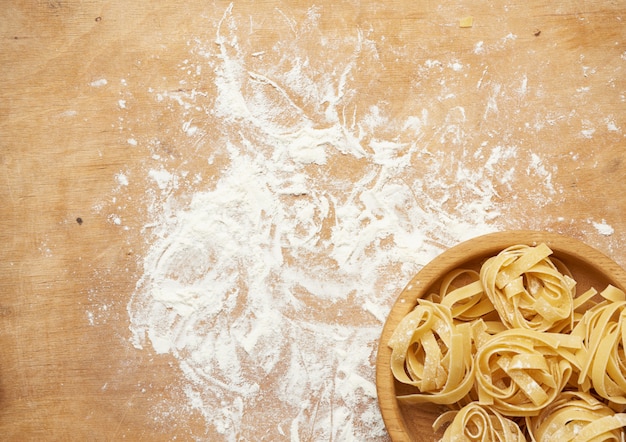 Ruwe fettuccine pasta op een bruin houten bord