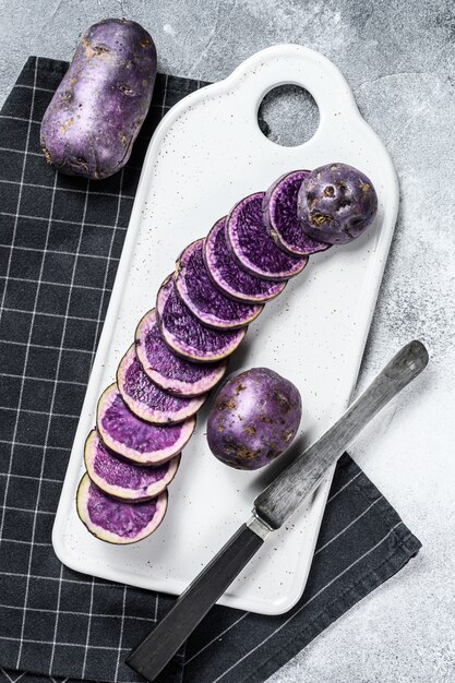 Ruwe gesneden violette aardappels op een wit hakbord. Bovenaanzicht