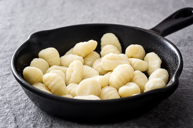 Ruwe gnocchi in gietijzeren koekenpan op grijze steen.