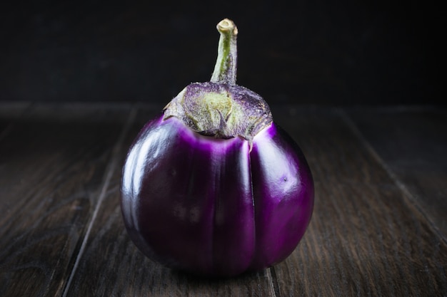 Ruwe paarse ronde aubergines op donkere rustieke houten tafel