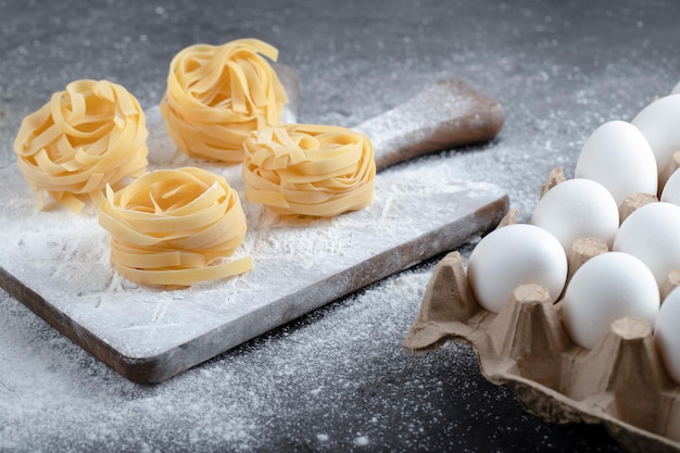 Ruwe tagliatelle nesten met bloem en rauwe eieren op zwarte ondergrond.