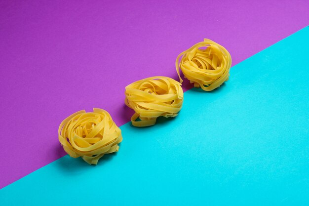Ruwe tagliatelle pasta geïsoleerd op een blauw en paars