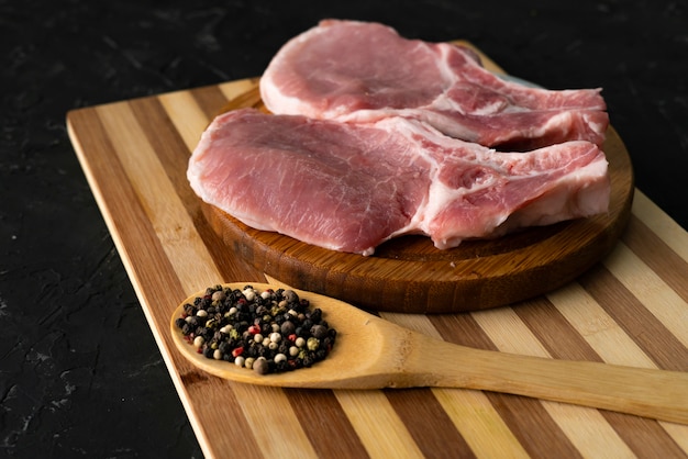 Ruwe varkensfilet op een snijplank, houten lepel met kruiden en peper, vet junkfood, ongekookt