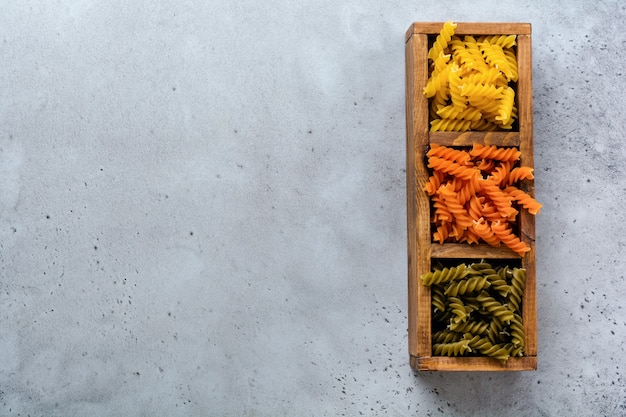 Ruwe veelkleurige drie kleuren fusilli pasta verspreid in houten kist op grijze betonnen ondergrond. bovenaanzicht.