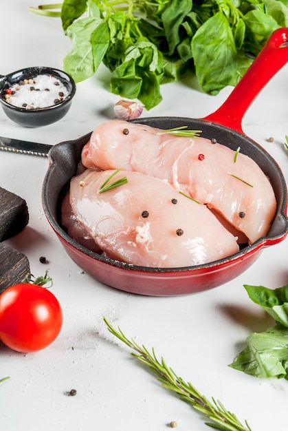 Ruwe verse kippenborstfilet met kruiden en kruiden voor het koken, in ijzer gegoten koekepan, witte marmeren lijst, exemplaarruimte