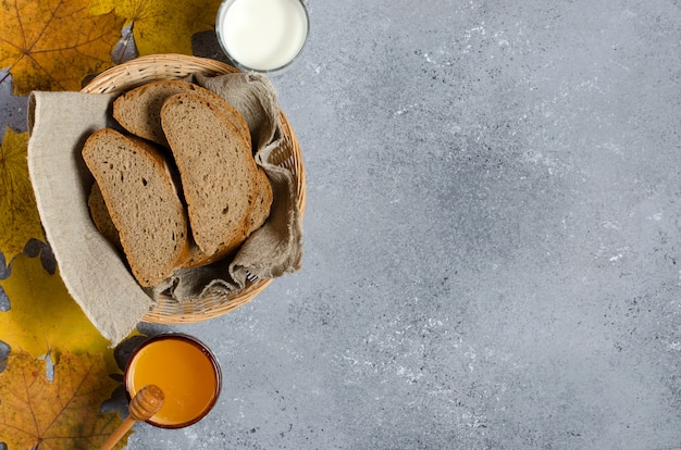 Il pane di segale viene tagliato a pezzi. miele, latte in una tazza di vetro, foglie di acero gialle.