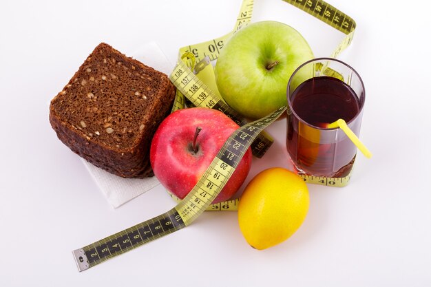 Rye bread with green and red apples and juice in a glass on a white plate with a yellow measuring ta...