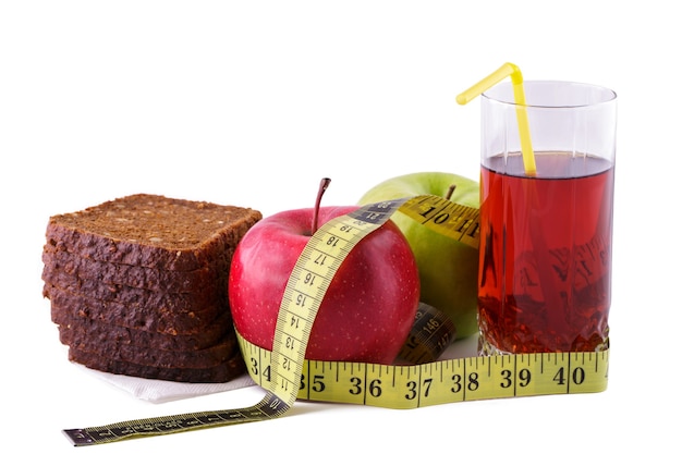 Rye bread with green and red apples and juice in a glass on a white plate with a yellow measuring tape