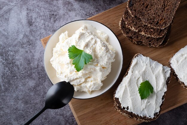 Rye bread on a wooden cutting board with curd cheese and ricotta and herbs Decorated with green herbs