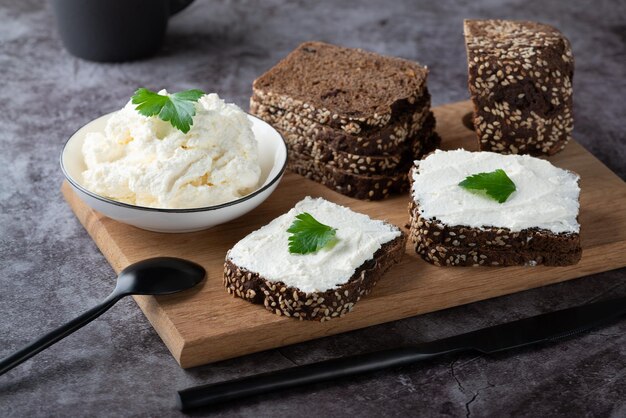 Rye bread on a wooden cutting board with curd cheese and ricotta and herbs Decorated with green herbs