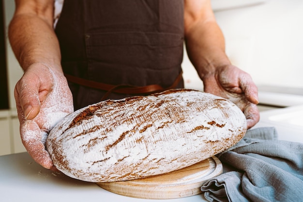 Photo rye craft homemade bread in muscular textured hands of male baker