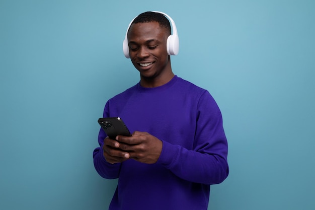 S donkere Amerikaanse man gekleed in een blauwe trui met koptelefoon en een smartphone